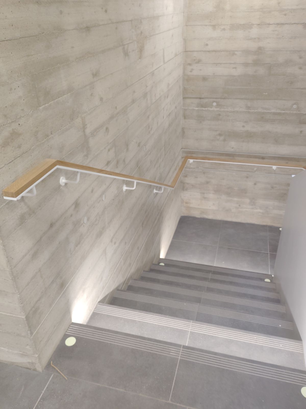Dřevěné madlo v bílém držáku na pohledovém betonu